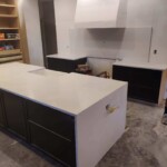 A modern kitchen island with a white countertop and dark cabinets in an unfinished kitchen space.