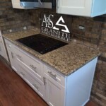Kitchen countertop with polished granite and white cabinetry.