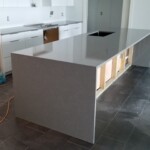 Modern kitchen island with a sleek gray countertop and open shelving.
