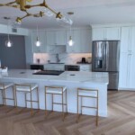 Modern white kitchen with island and gold-accented lighting.