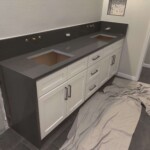 Modern bathroom vanity with dual sinks and dark countertop.