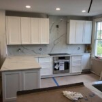 Modern kitchen with white cabinetry and marble countertops.