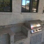 Outdoor granite BBQ grill and seating area under windows.