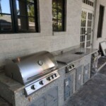 Outdoor stainless steel grill setup with stone counter and storage.