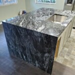 Modern kitchen island with black and white marble countertop and waterfall edge.