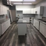 Modern kitchen with white cabinets and a central island on dark wood flooring.