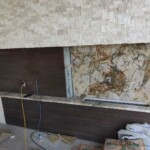 Partially installed kitchen backsplash with granite and dark wood panels.