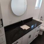 Modern bathroom vanity with black countertop and white cabinets.