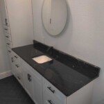 Modern bathroom vanity with black countertop and round mirror.