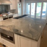Polished marble kitchen island with modern appliances and large windows.