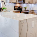 Modern kitchen with sleek white marble countertops and stainless steel appliances.
