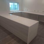 Modern kitchen island with sleek white countertop and light wood cabinetry.