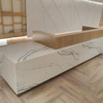 Modern white marble bench with wooden accents on a wooden floor.